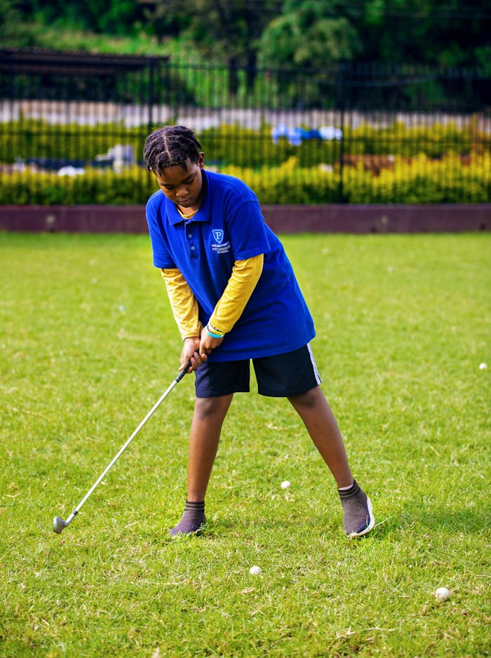 A young boy in a blue polo shirt playing golf on a sunny day outdoors.