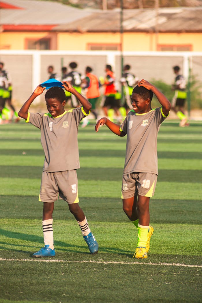 Two young soccer players enjoying training on a sunny day with their team in the background.