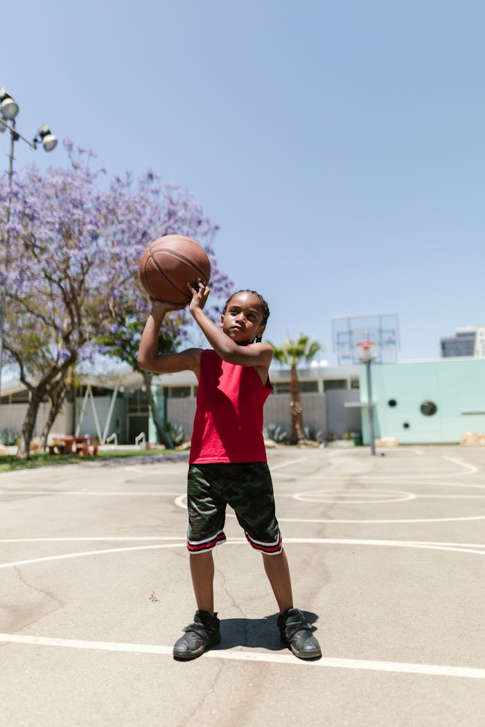 A young boy having fun on a basketball court under a clear sky, holding a basketball.